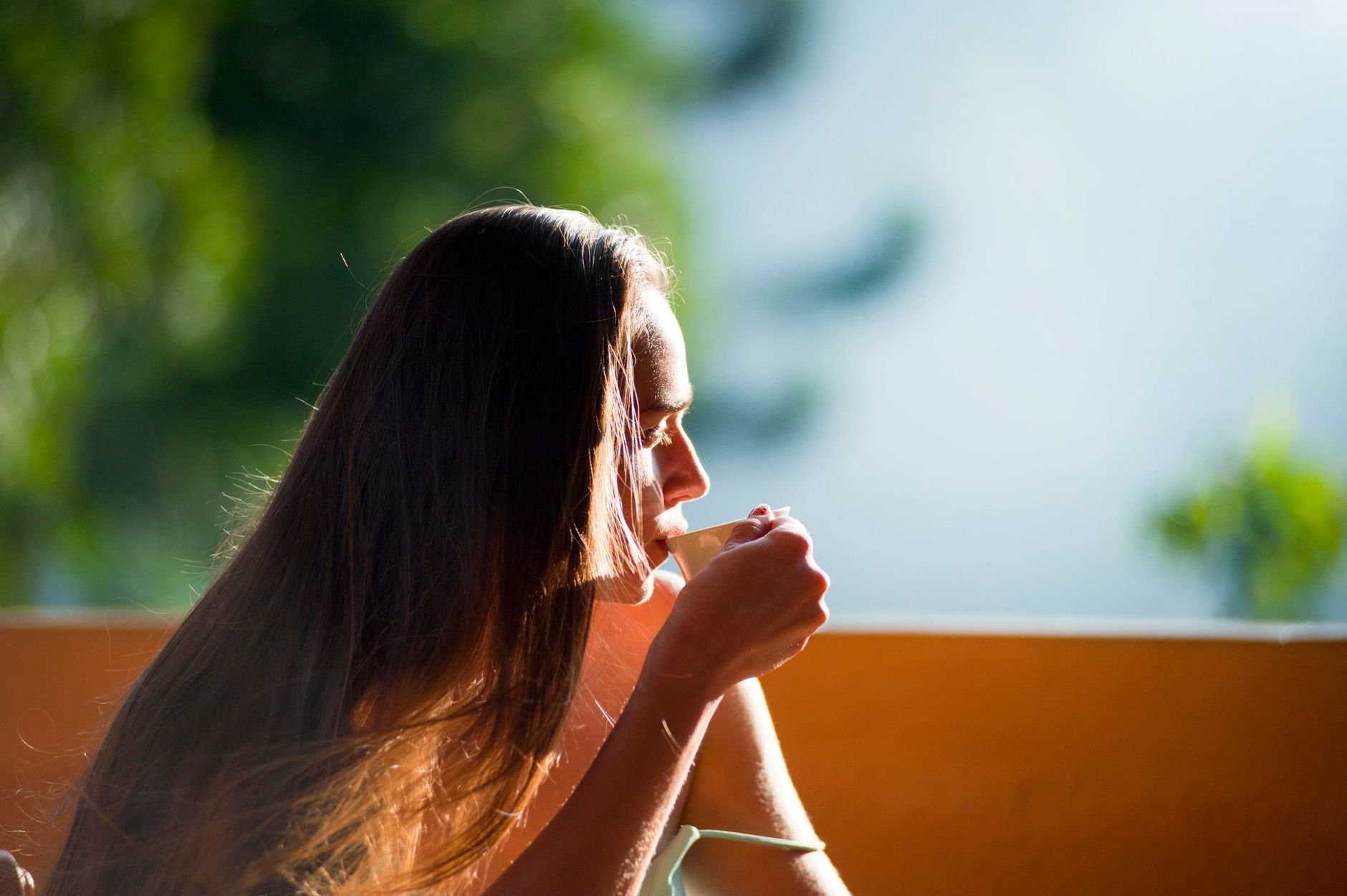 A woman peacefully sipping tea outdoors in the morning sunlight.
